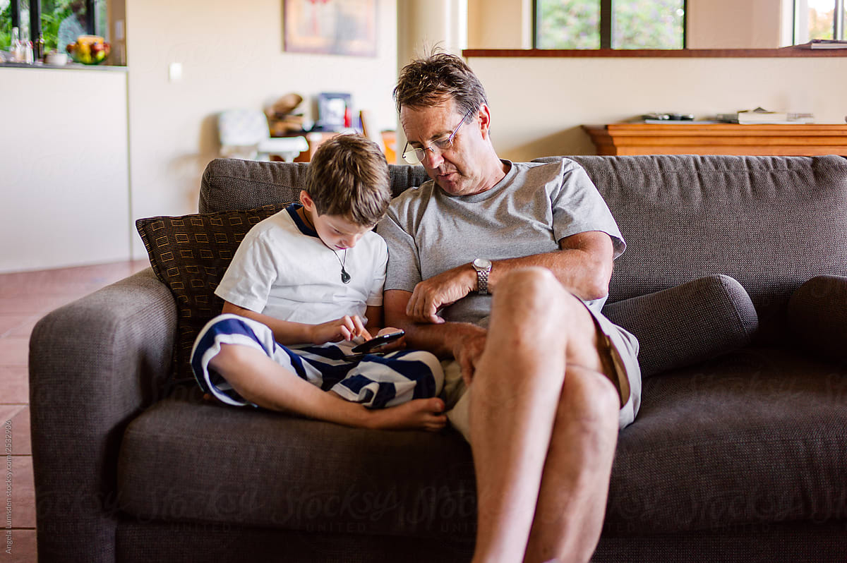 Grandfather and grandson talk tech devices on a couch indoors