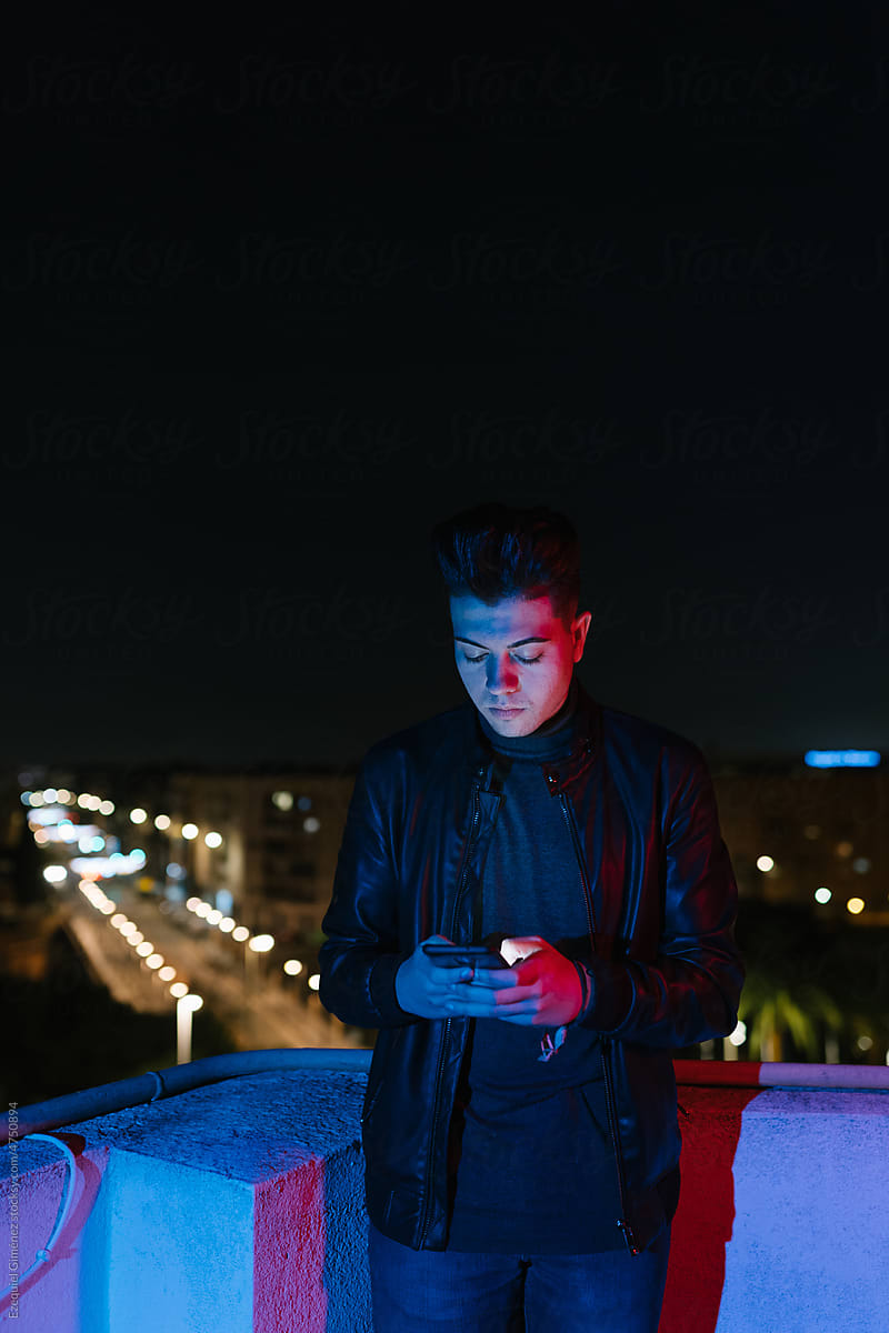 Trendy guy standing on terrace and using smartphone