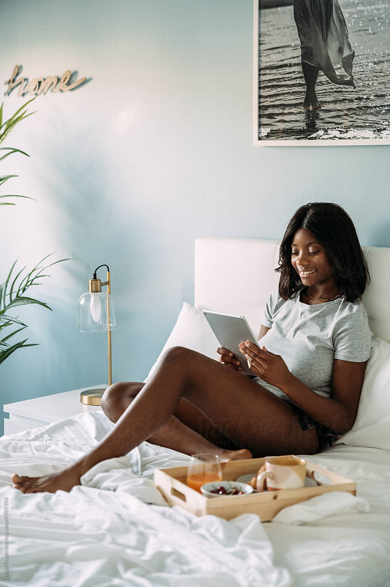 Black woman browsing tablet on bed