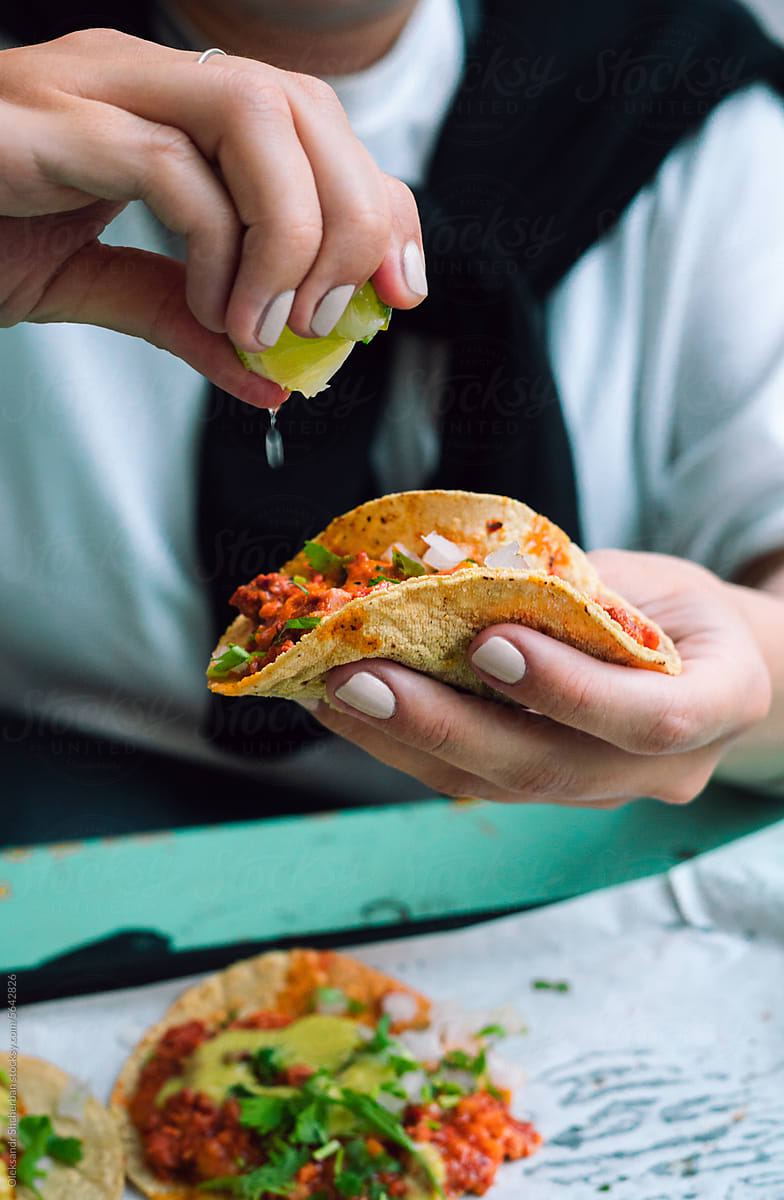 Woman holding taco and squeezing line on it, tacos close up