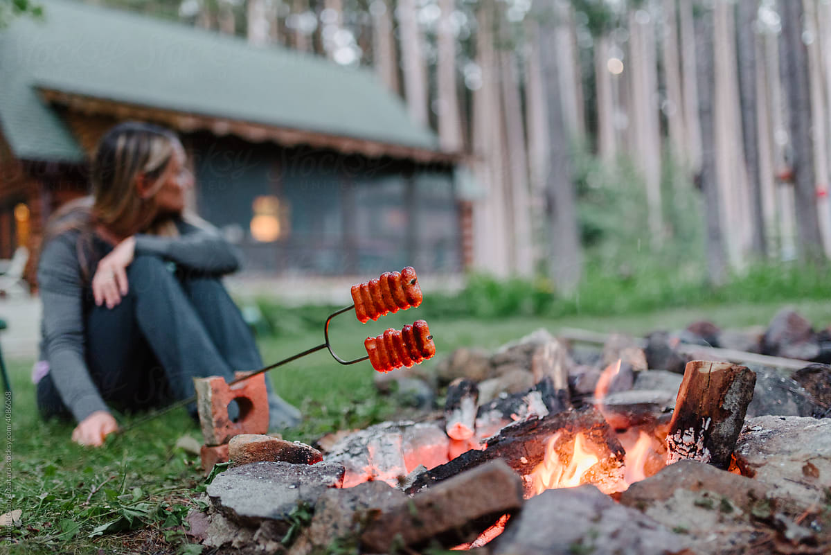 Woman roasting sausages over a campfire