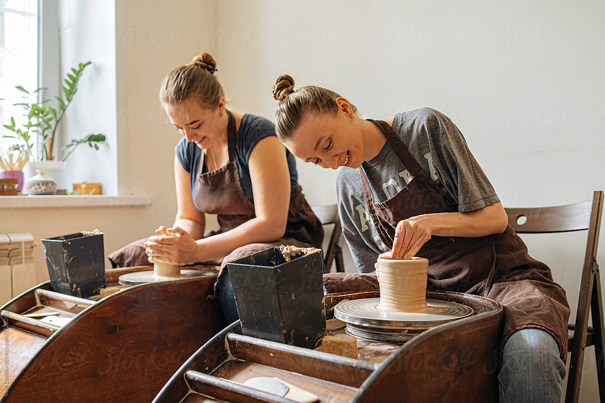two young women having fun working behind a potter\'s wheel