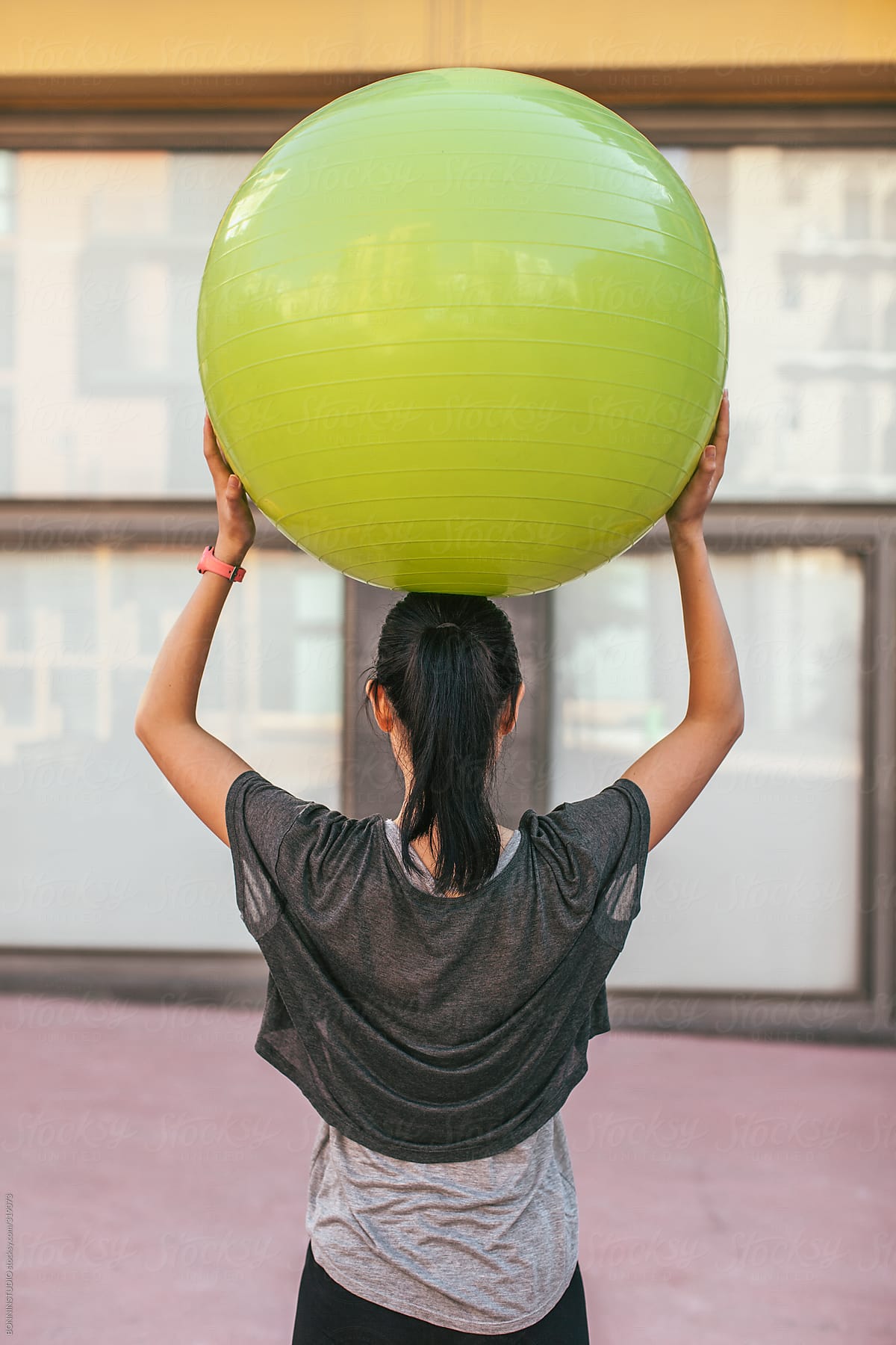 Asian fitness woman training on the street with a green Pilates ball.