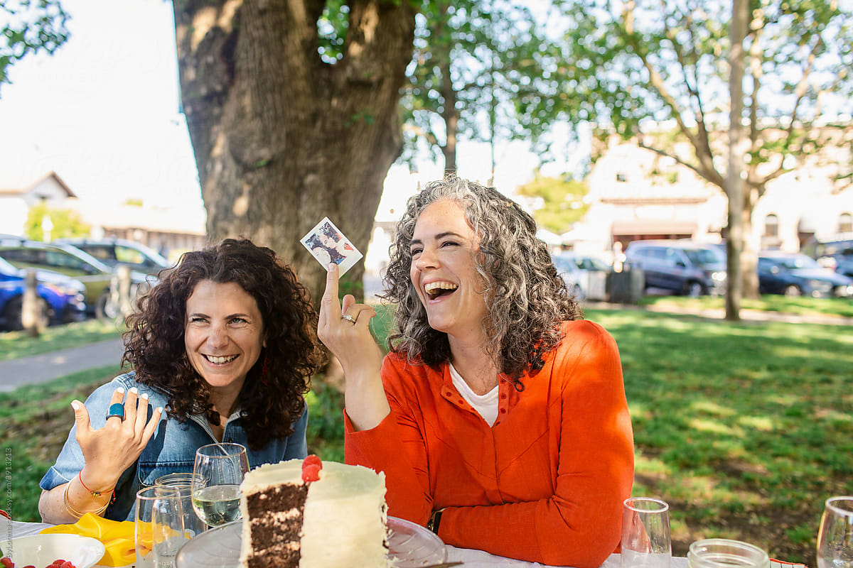 Adult friends showing instant photo by cake in garden party