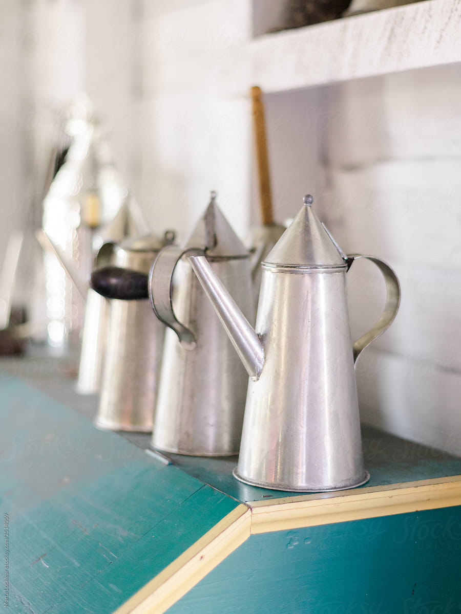 Row of handmade tin tea kettles on a bright turquoise shelf