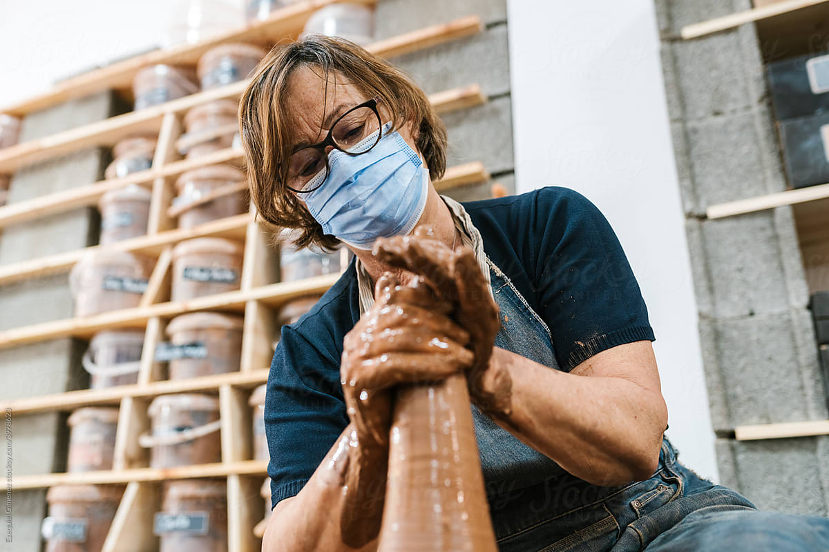 Mature female artisan in mask creative clay vessel
