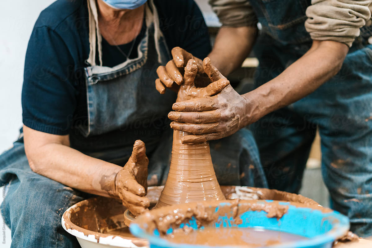 Crop potters making clay vase on wheel together