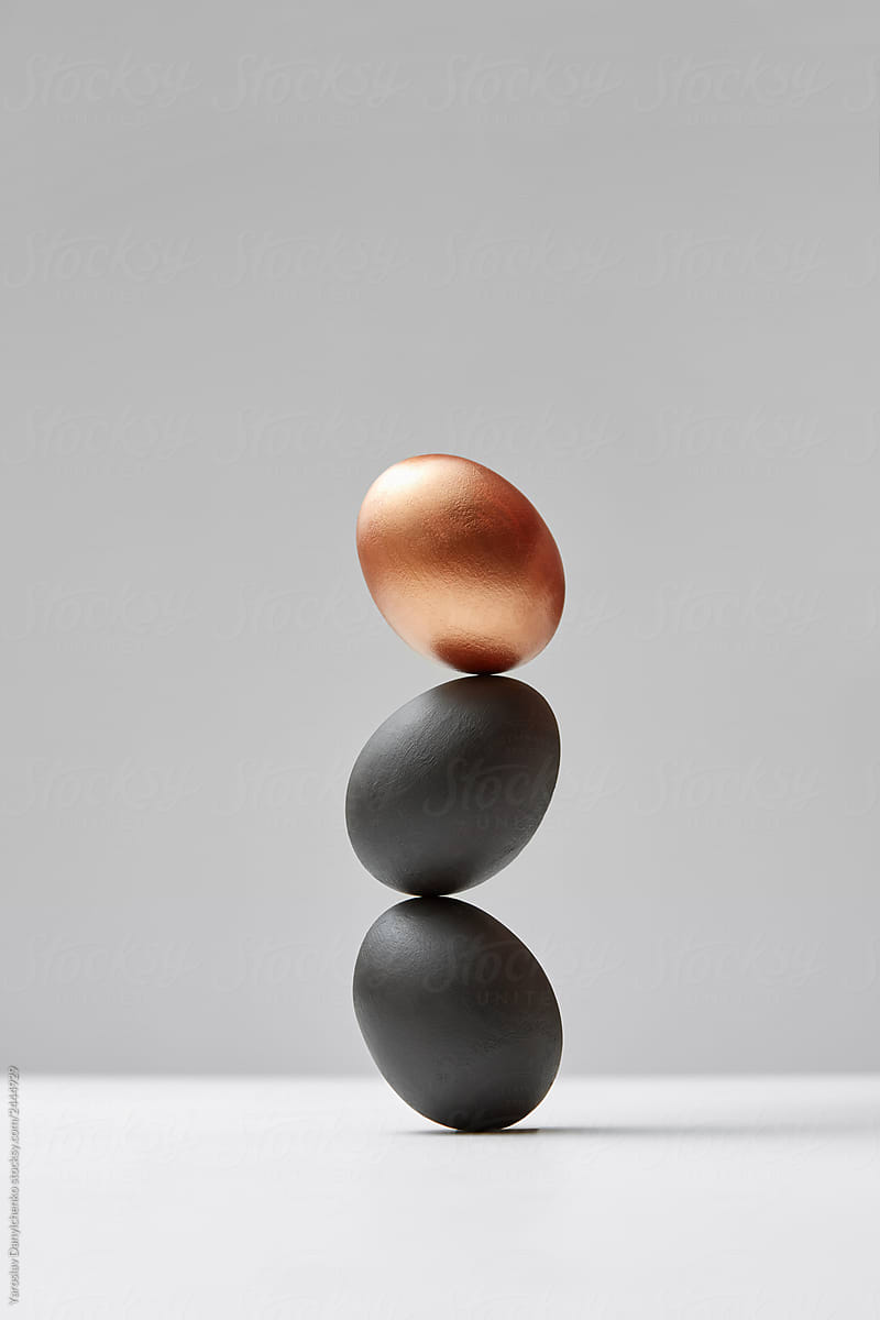 Vertical column from colored eggs black and golden on a gray background. Easy enrichment concept.