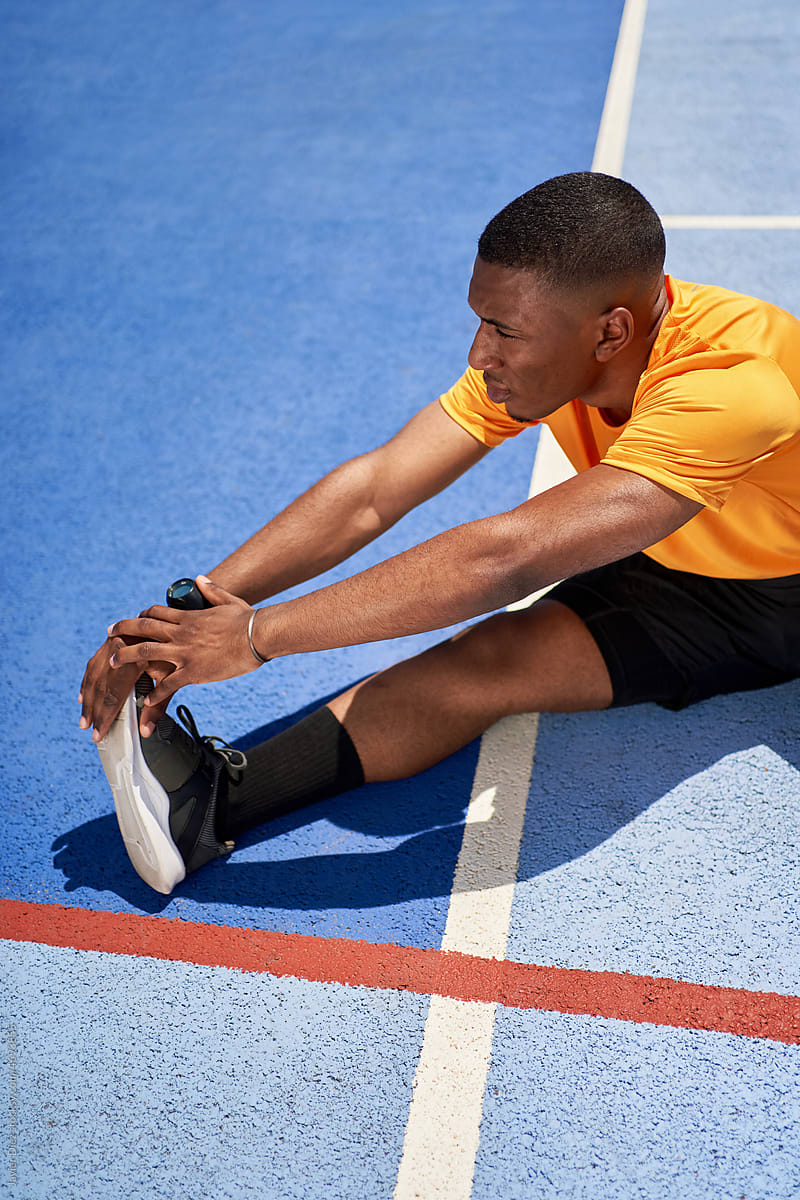 Athletic young black guy stretching legs at stadium