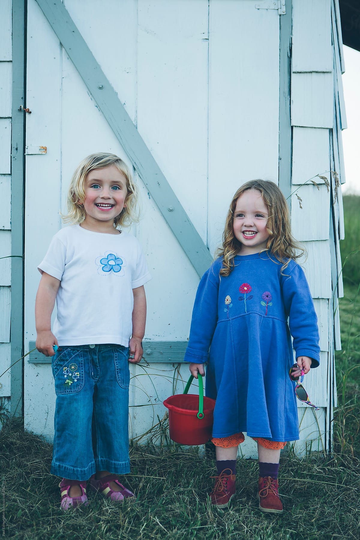 Portrait of two three year old girls smiling, standing outside barn