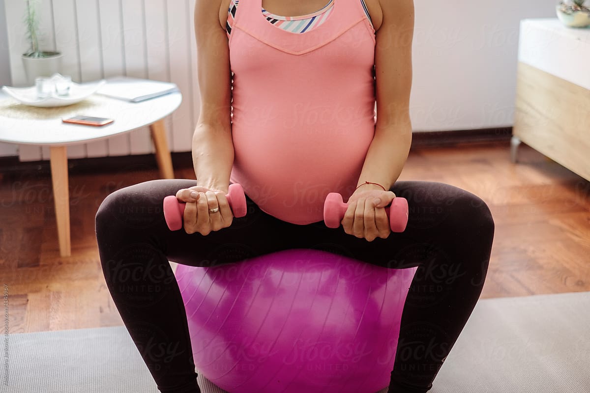 Anonymous Pregnant Woman Sitting On The Pilates Ball And  Exercising With Weights