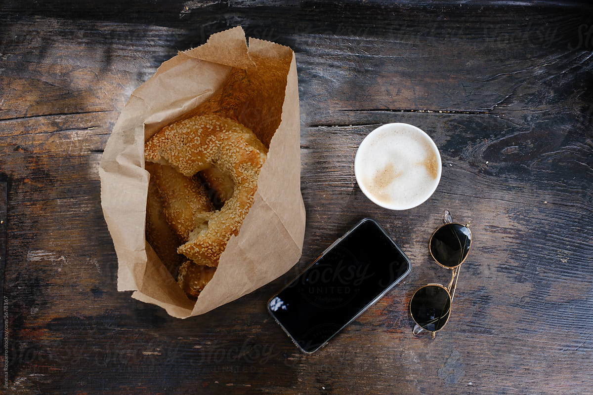 Bagels, coffee, smartphone and sunglasses on wooden table