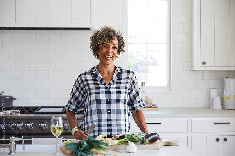 African American woman laughing and cooking in the kitchen with white wine