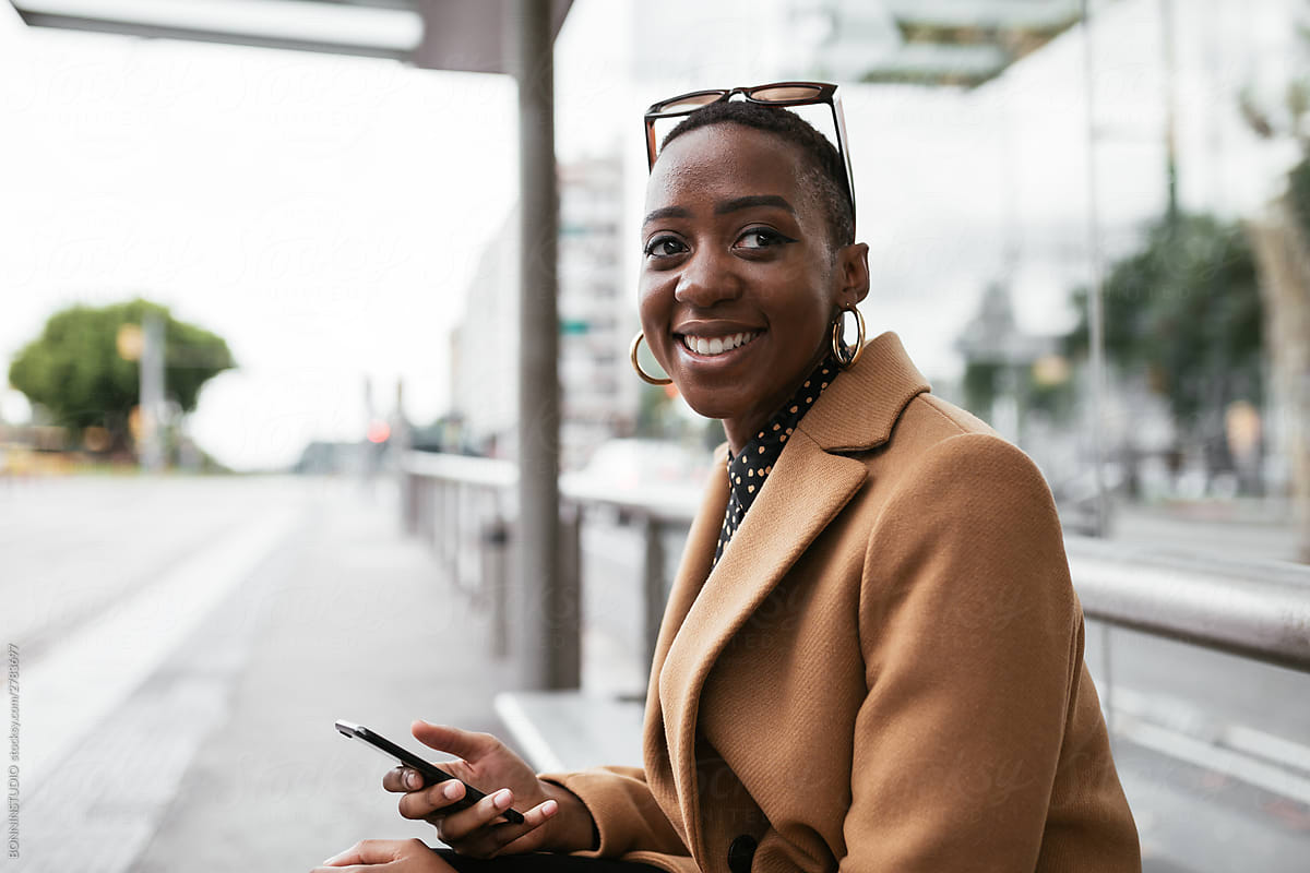Cheerful African American female using smartphone on bus station