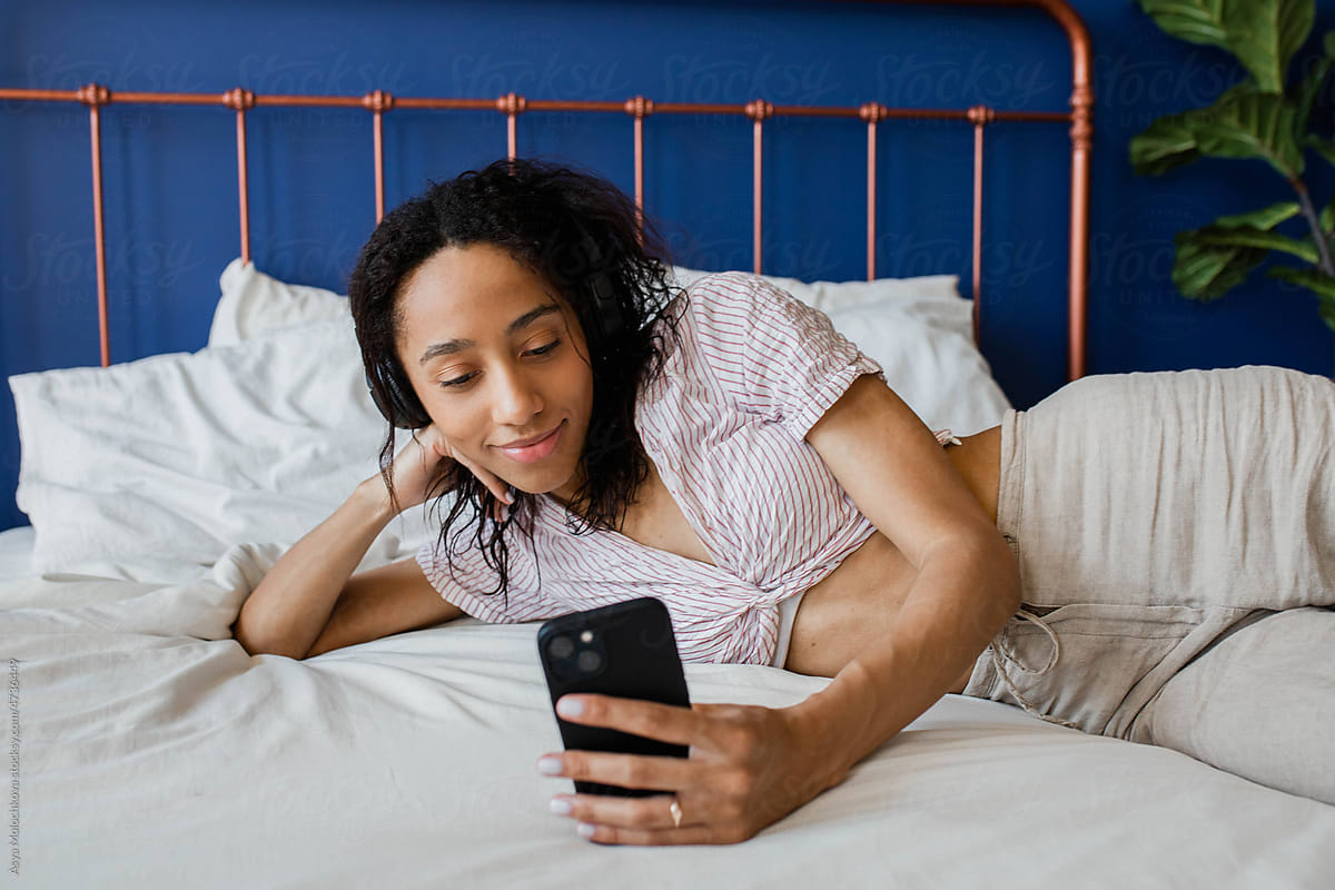 Young woman lying on the bed holding mobile phone and smile