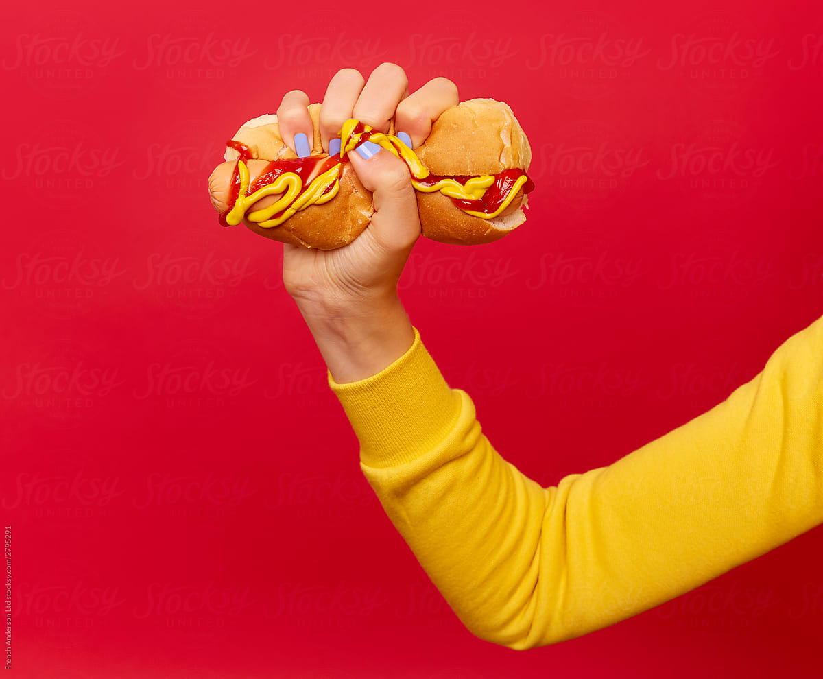 Hand with blue painted nails squeezes hotdog