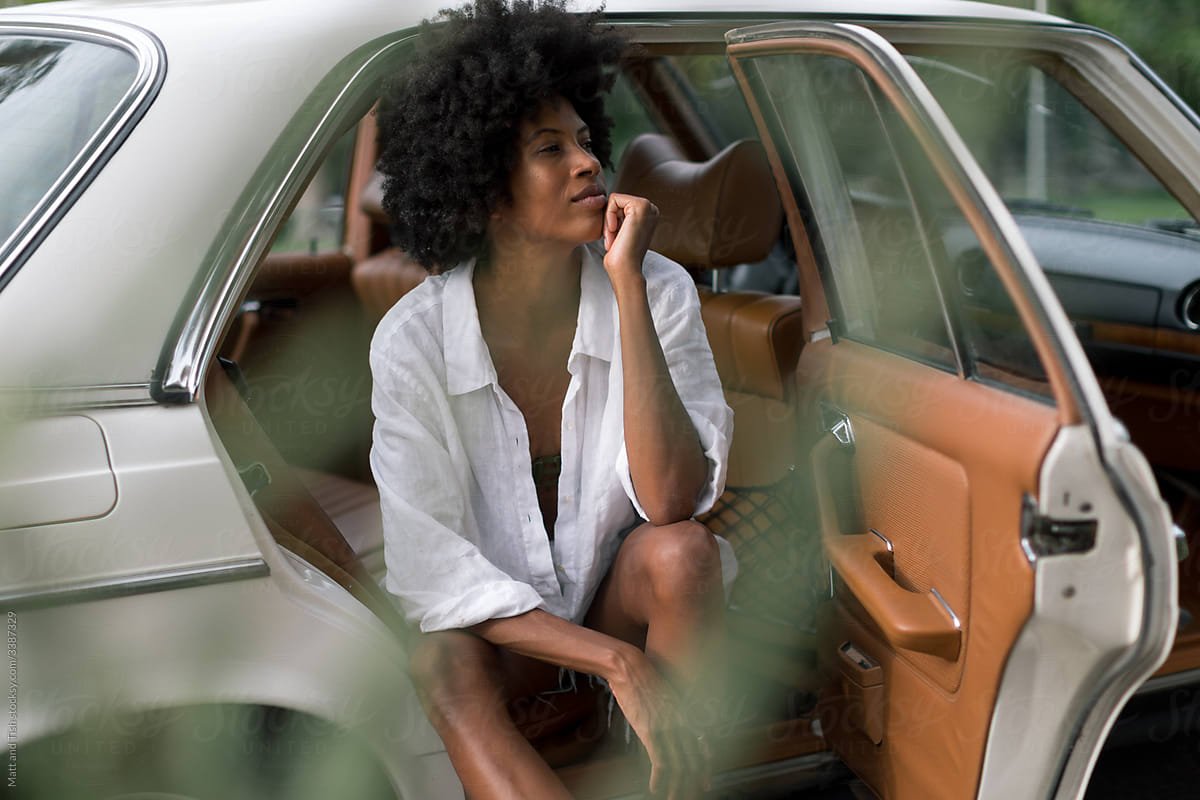 Black Women sitting in White Vintage Car with her Feet on Curb.