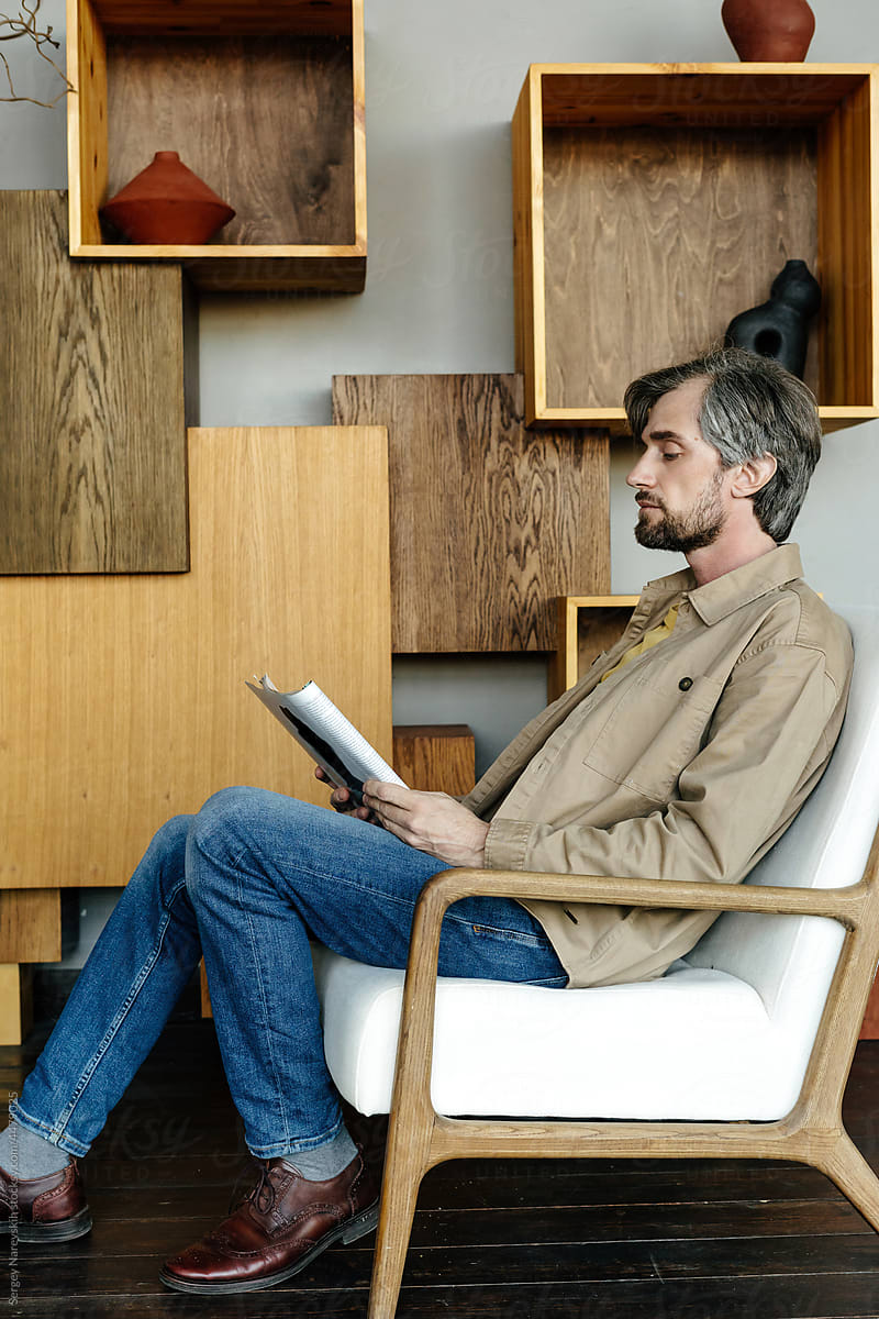 Man reading magazine in armchair in modern room