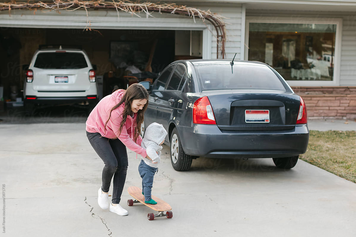 A Mom and Baby Play on Skateboard in Driveway