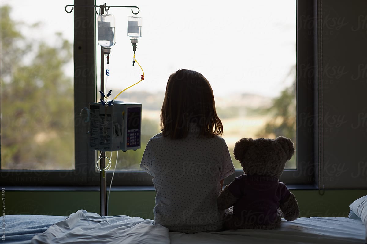Silhouette of a child patient with teddy bear on bed in hospital room