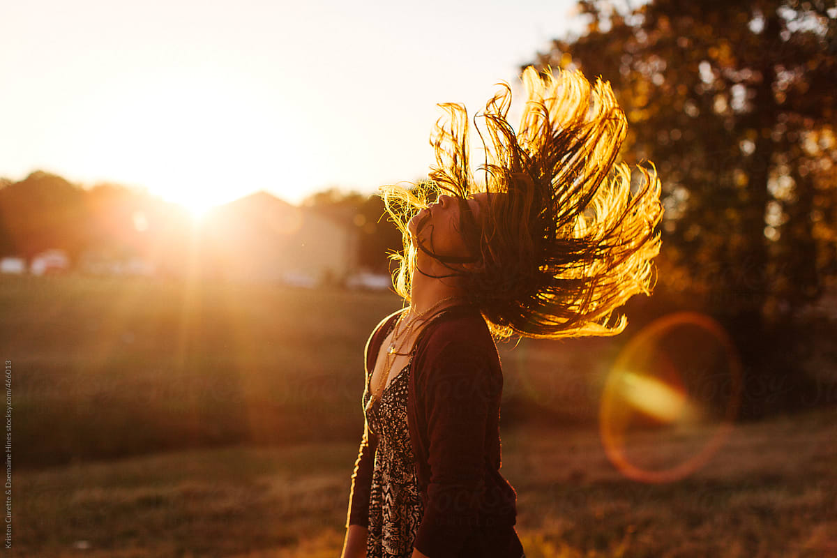 A woman flipping her hair during sunset in an open field.