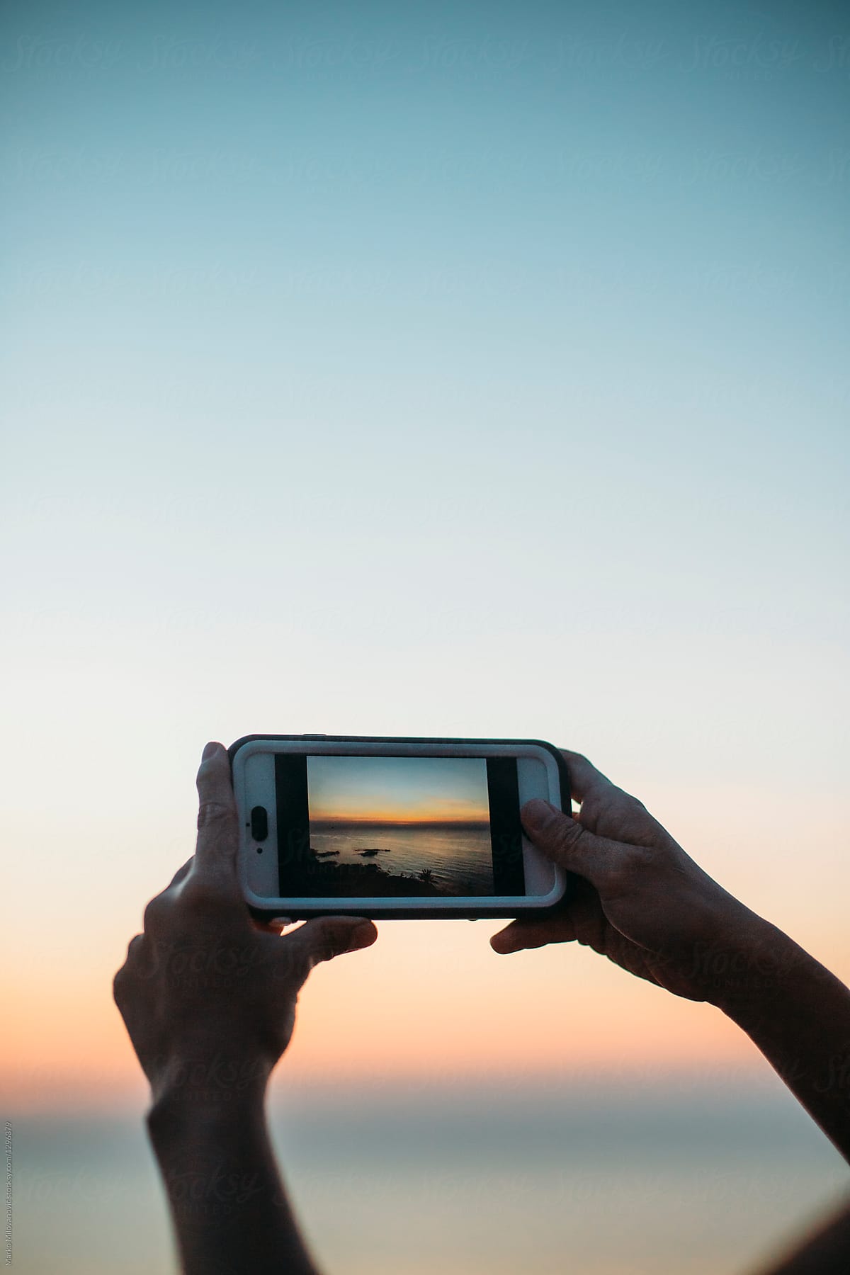 Woman taking pictures with phone at sea sunset