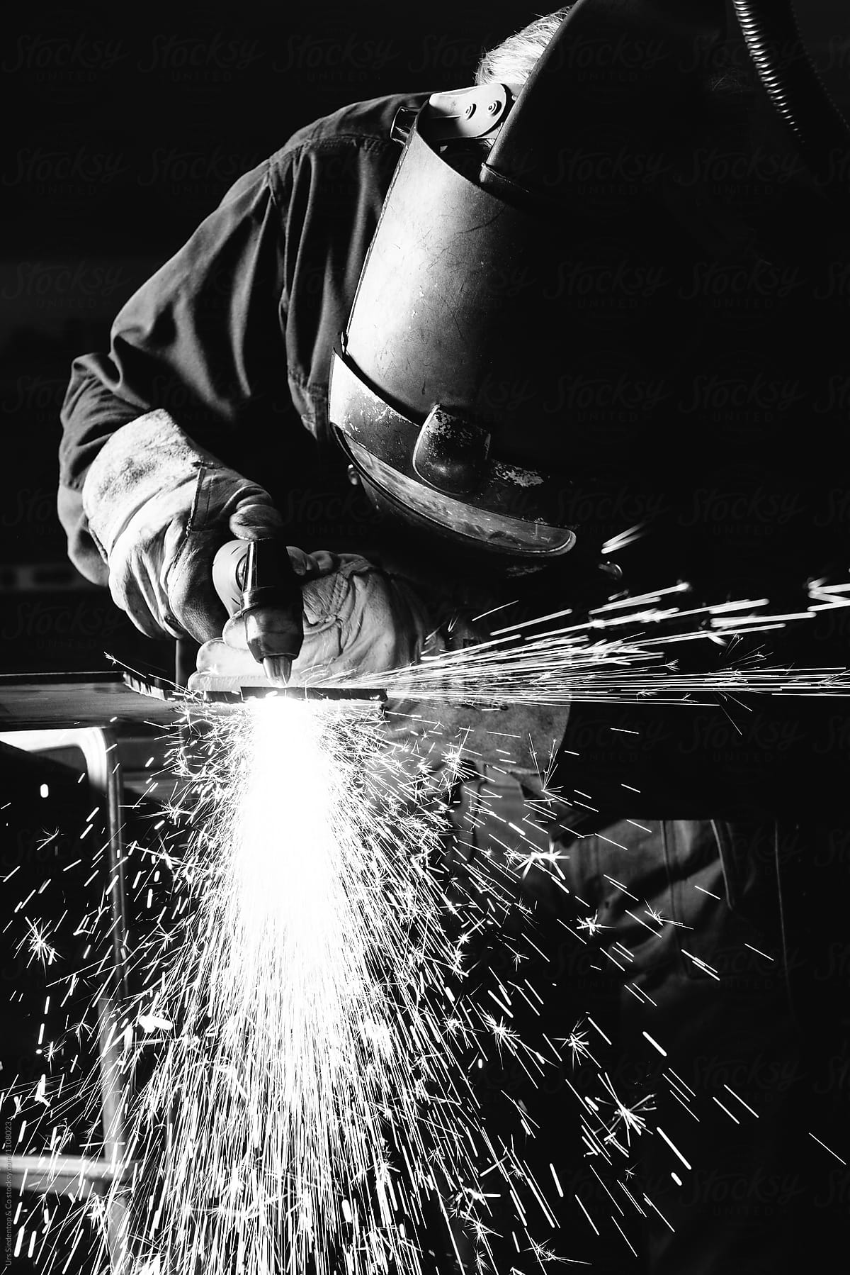 Close up black and white image of steel worker cutting iron with