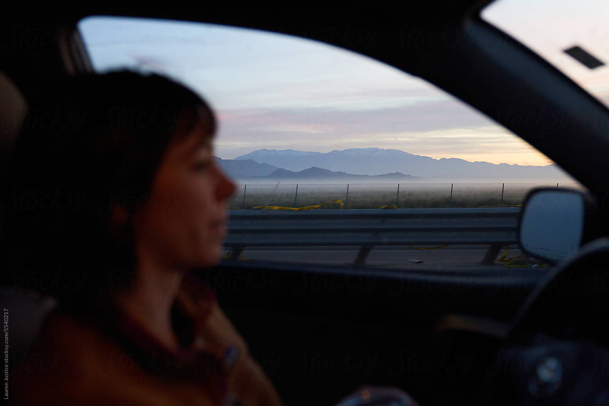 A girl drives by mountains at sunrise