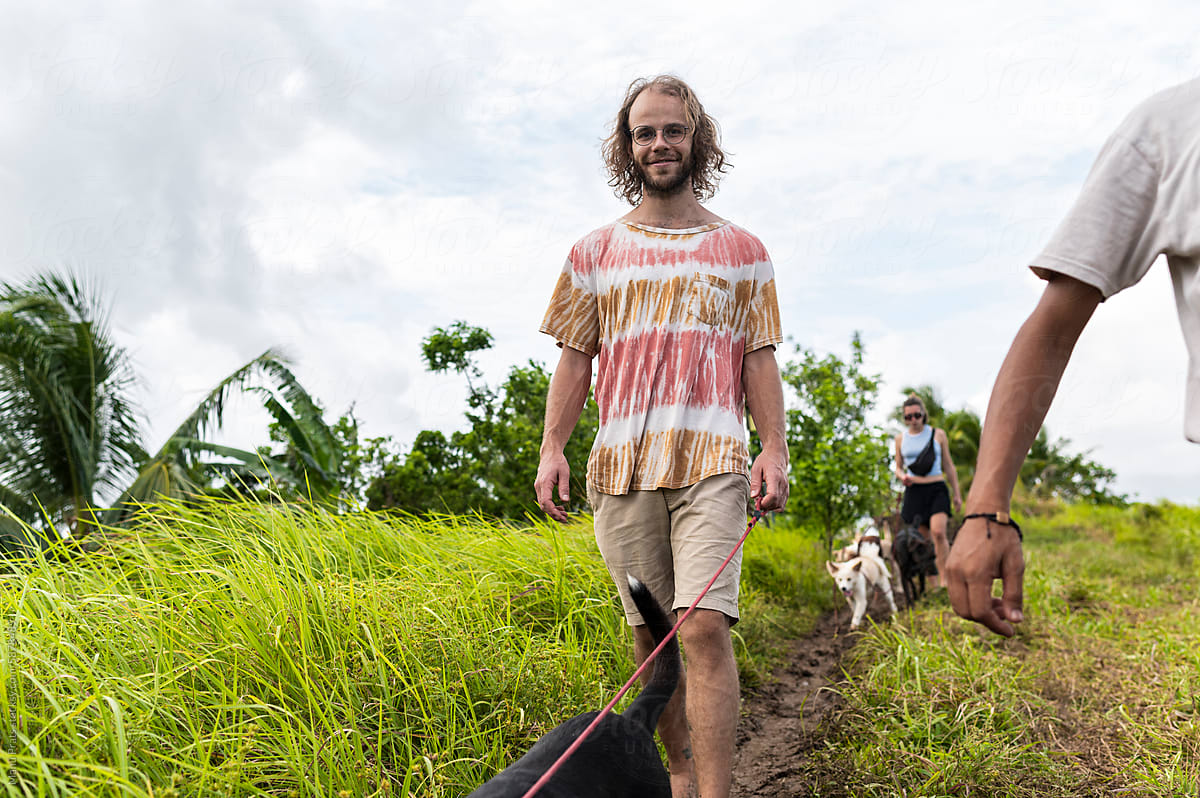 Activist volunteer friends walking rescued dogs by tropical pathway