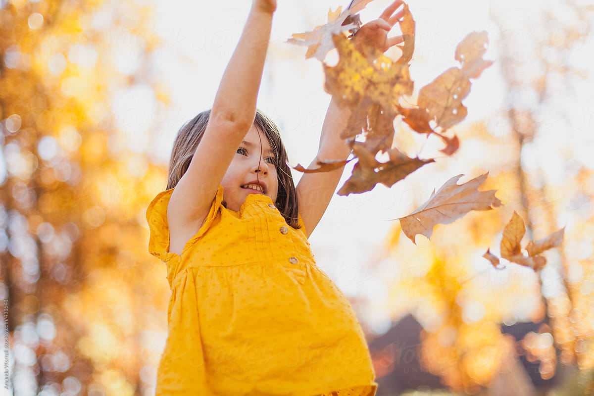 Smiling girl wearing gold top throws leaves in air