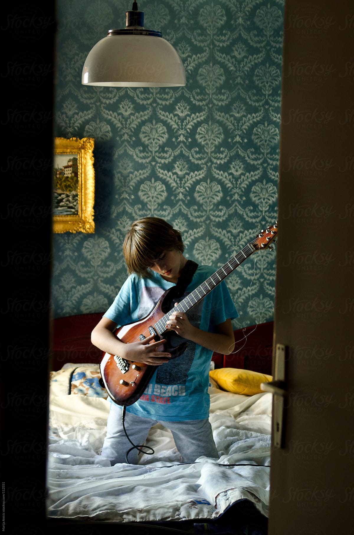 Boy is playing electric guitar in retro room of his parents
