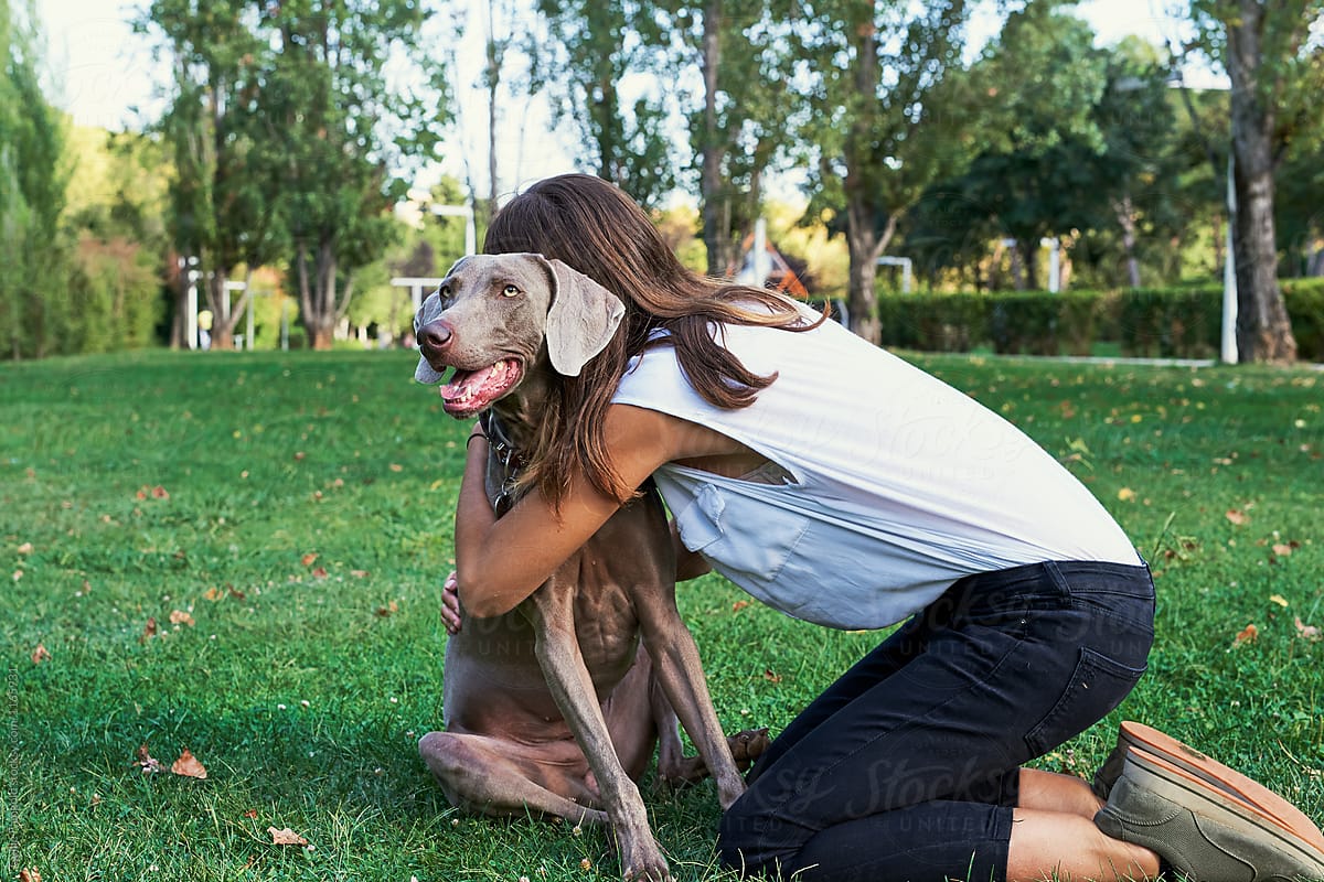 Unrecognizable girl hugging her dog in park.