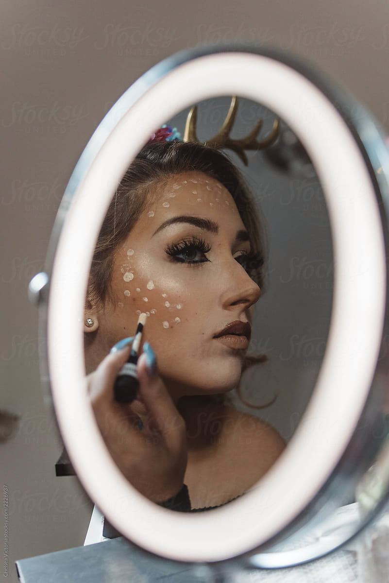 A girl in her twenties putting on makeup her bedroom for halloween