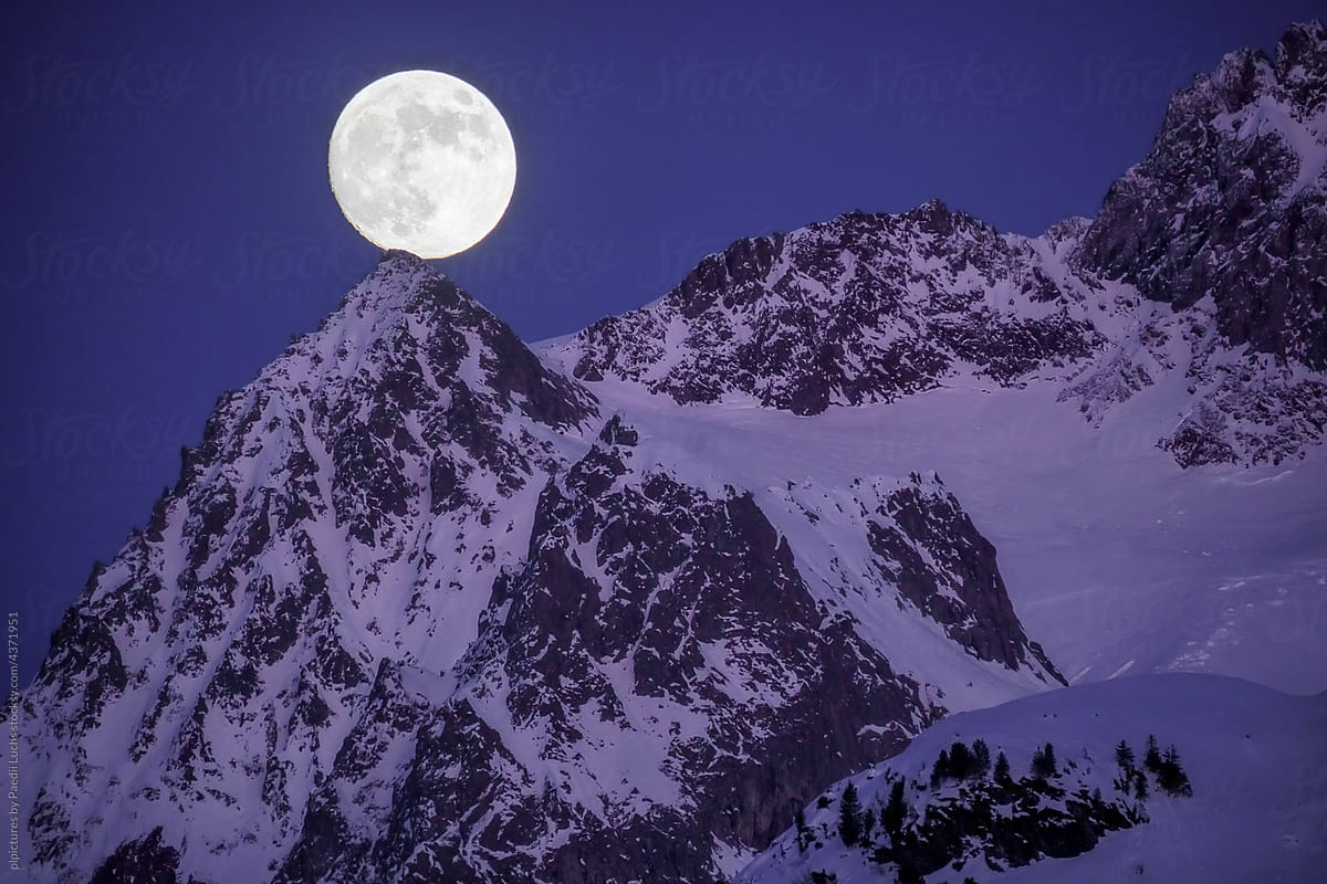 Full moon over snowy mountain peak.
