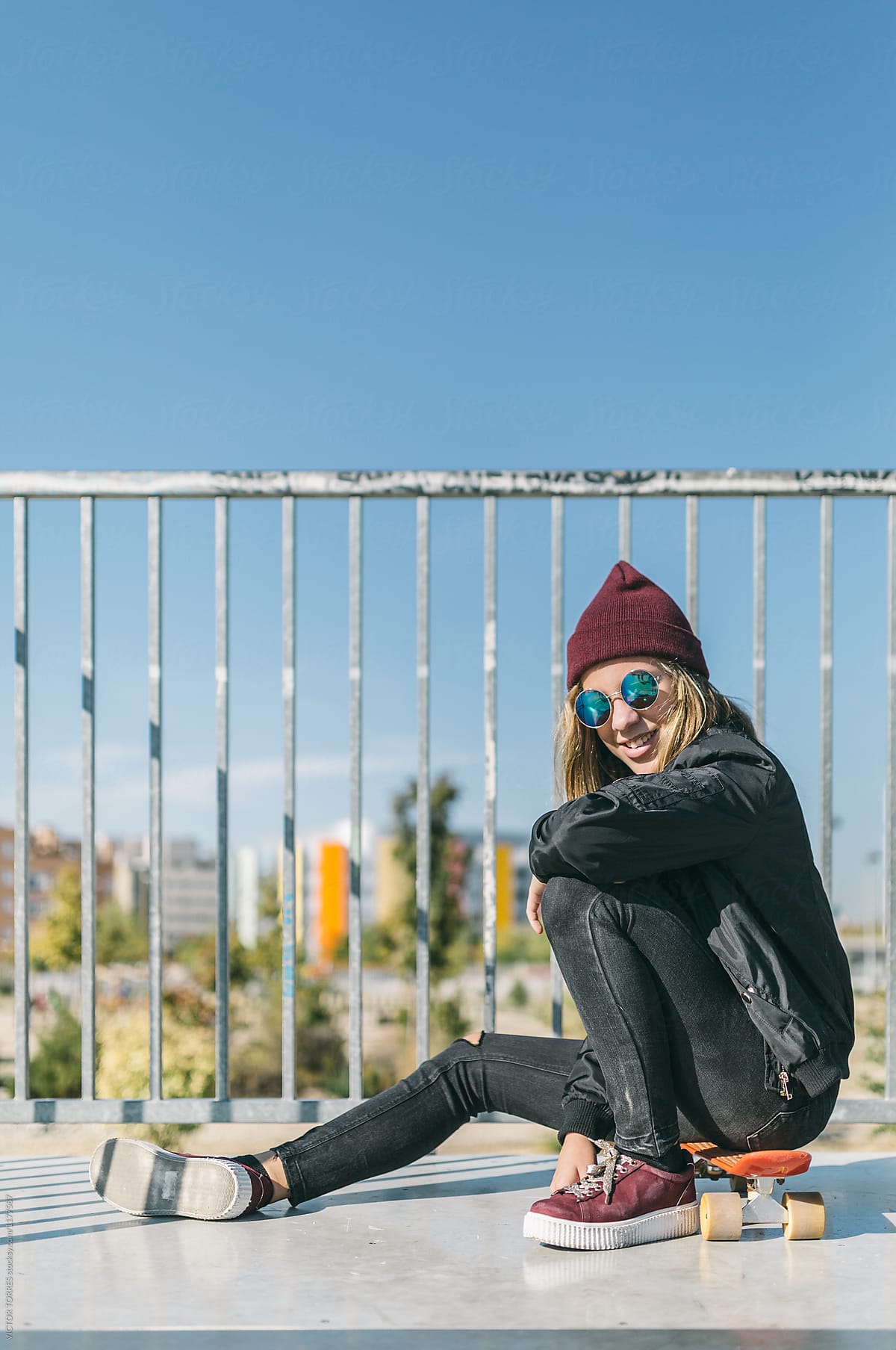 Smiley teen-age girl sitting on skateboard.