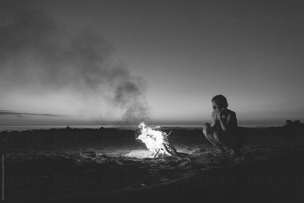 Woman enjoying the warmth of a bonfire on the beach under the stars.