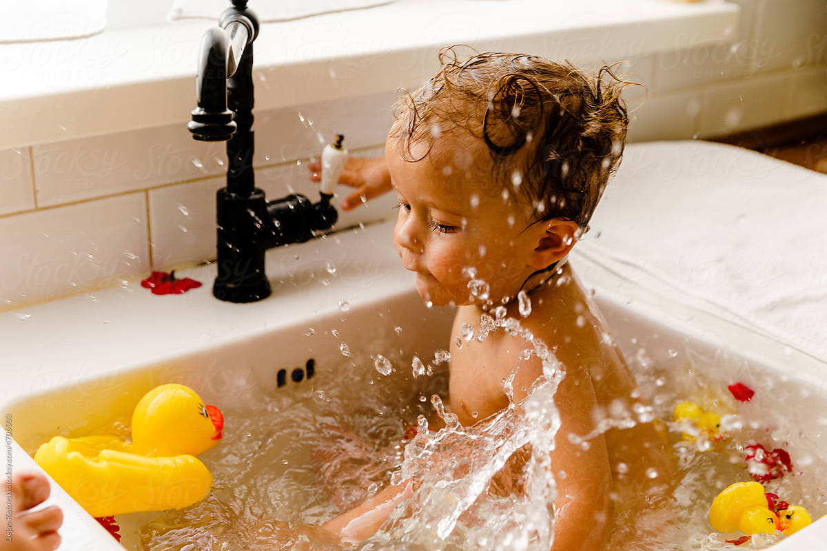 Baby playing with ducks in the kitchen sink