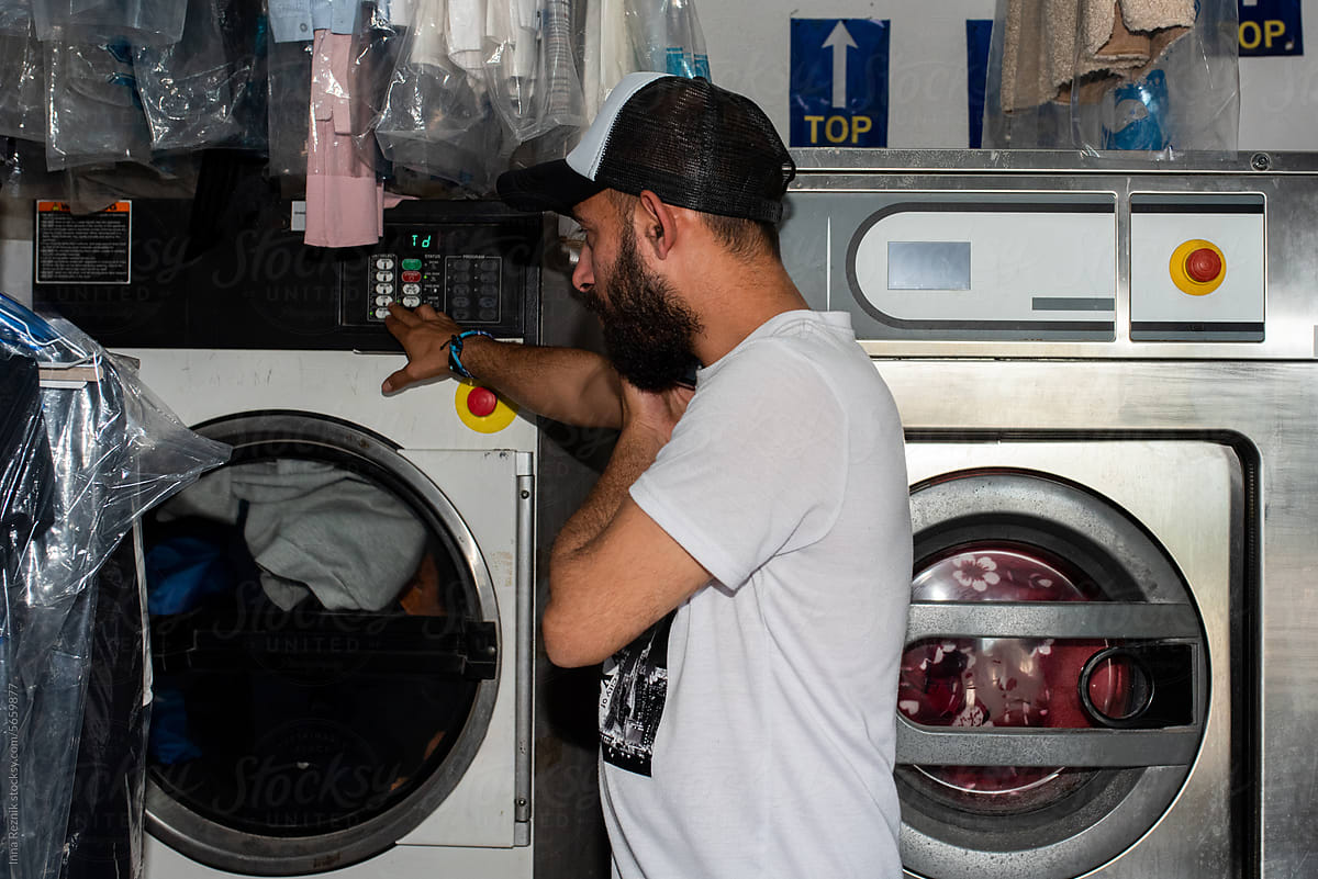 Man Operating Laundry Machines While Talking on Mobile Phone.