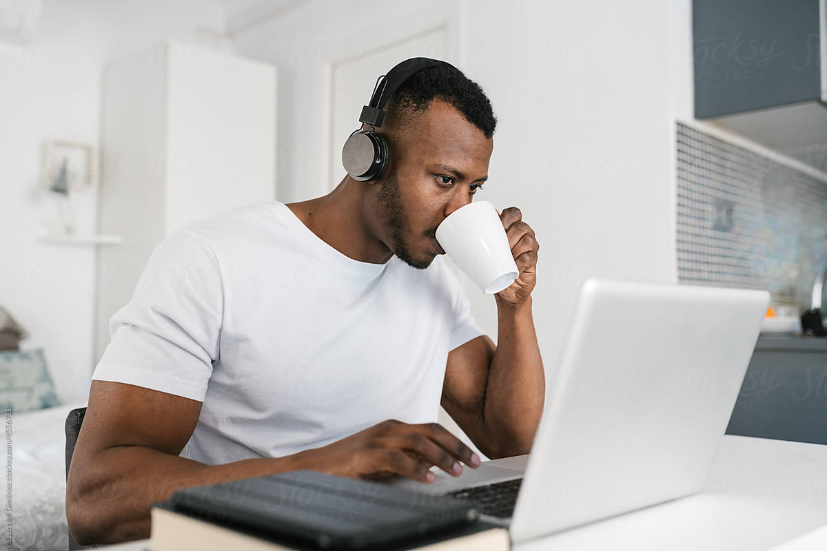 Black male freelancer drinking coffee and using laptop