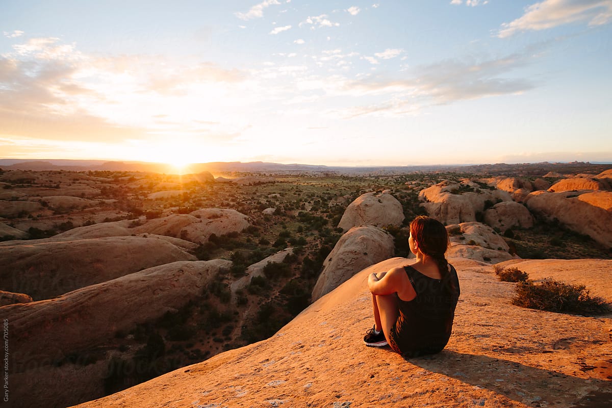 A girl watching the sun set on the top of a rock in Utah after a run