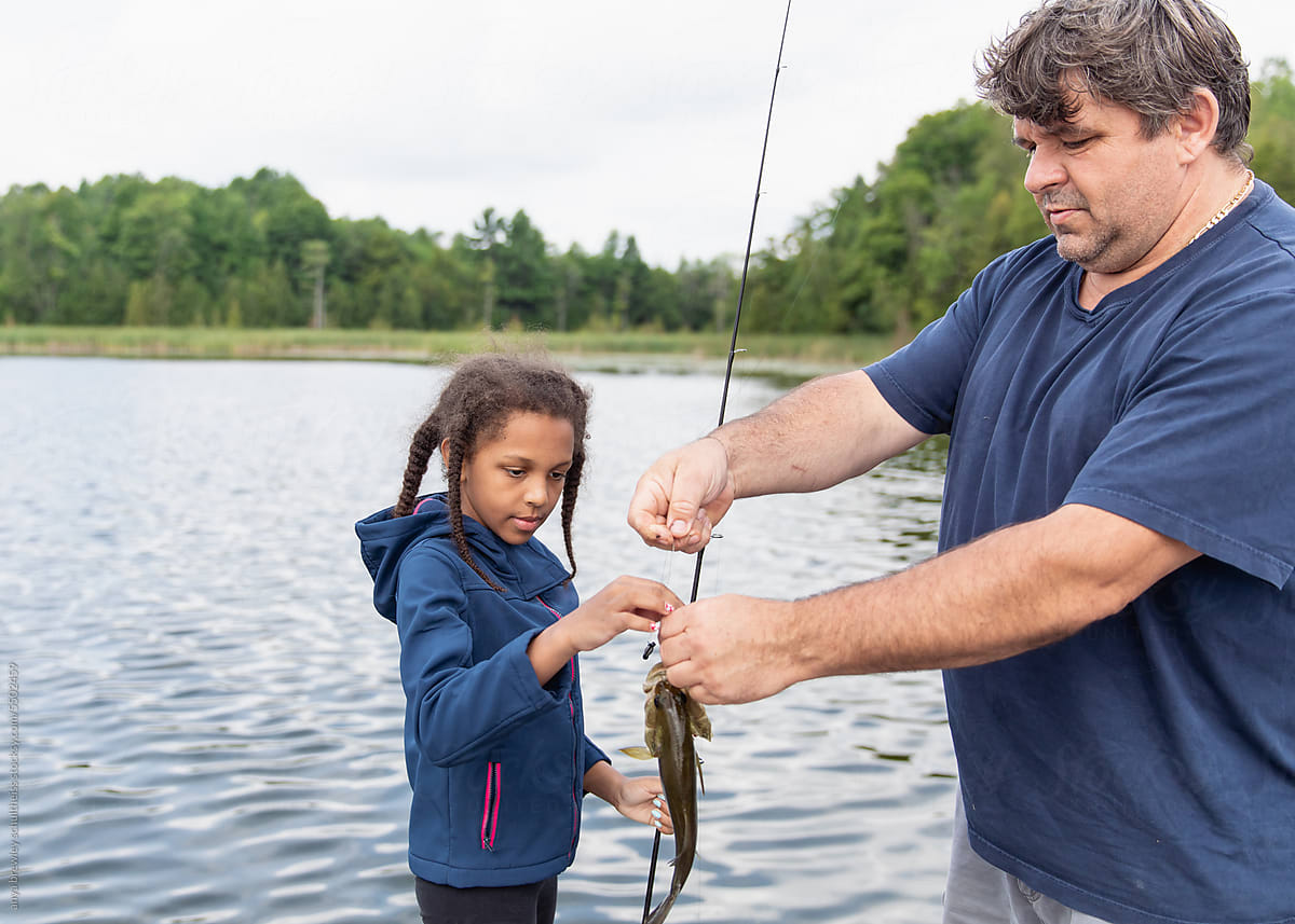Father helping his child to remove a caught fish from her fishing hook