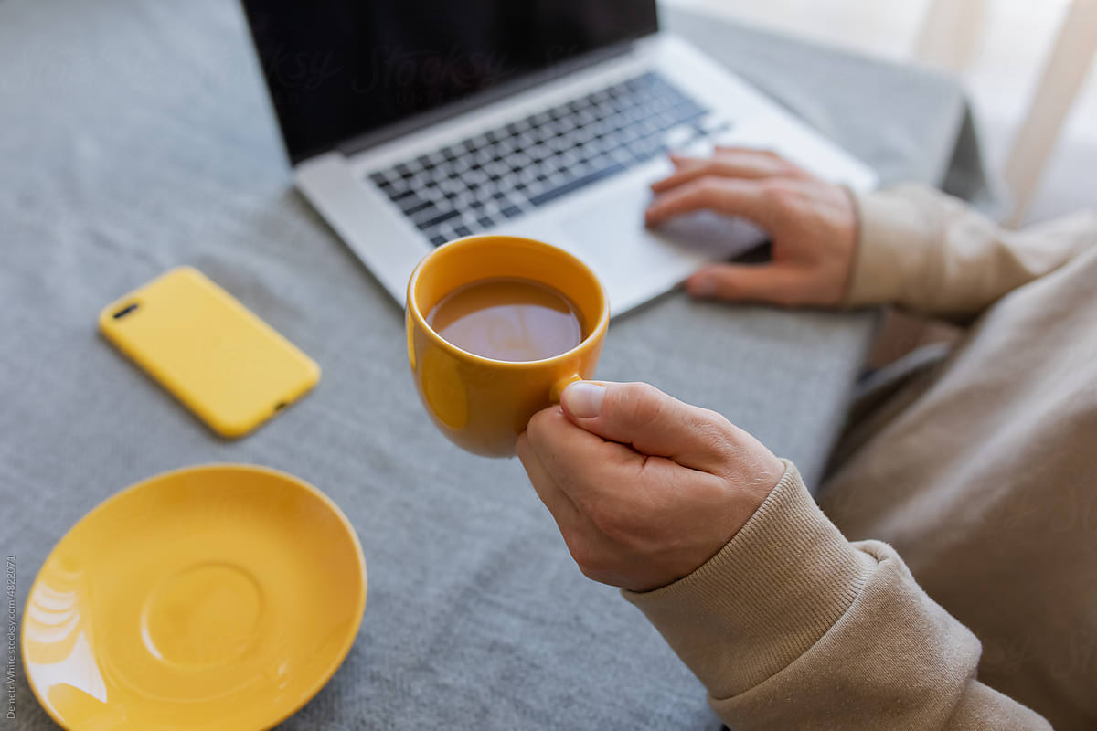 a mug with coffee in a man\'s hand in the background a laptop
