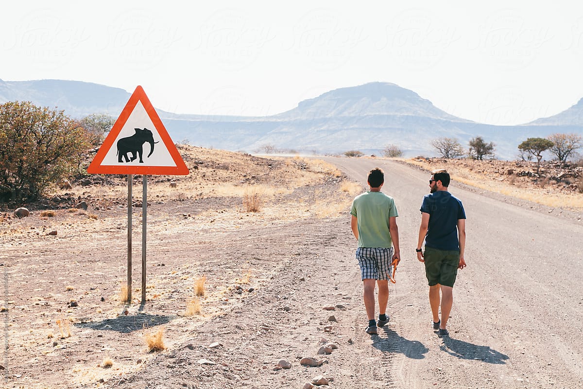 Two young men walking on the side of an African dirt road with an Elephants crossing warning sign