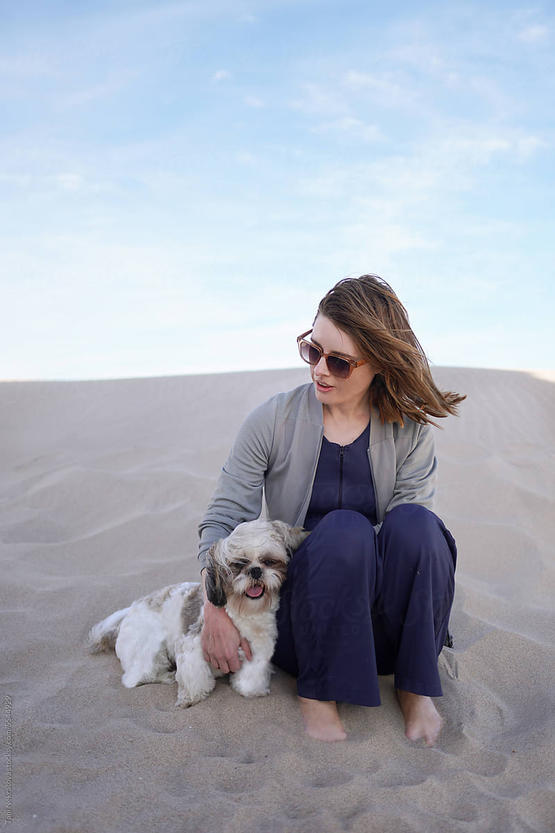 A woman cuddles a shih tzu dog in the sand