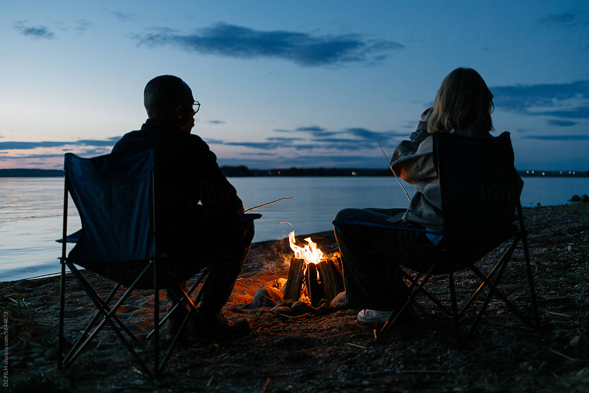A man and a woman are sitting around a campfire