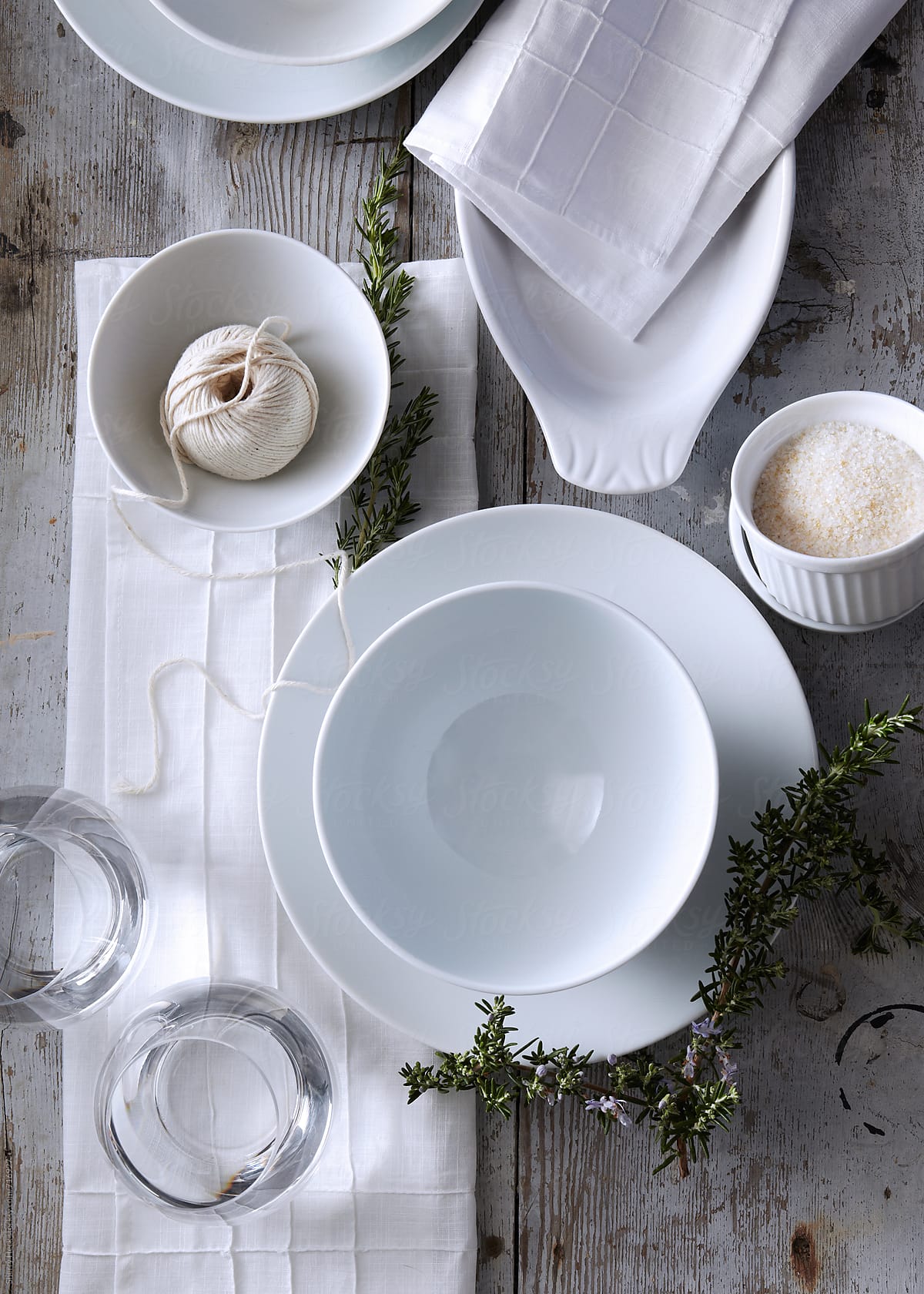 White plates and bowls with rosemary spring on white wood surface