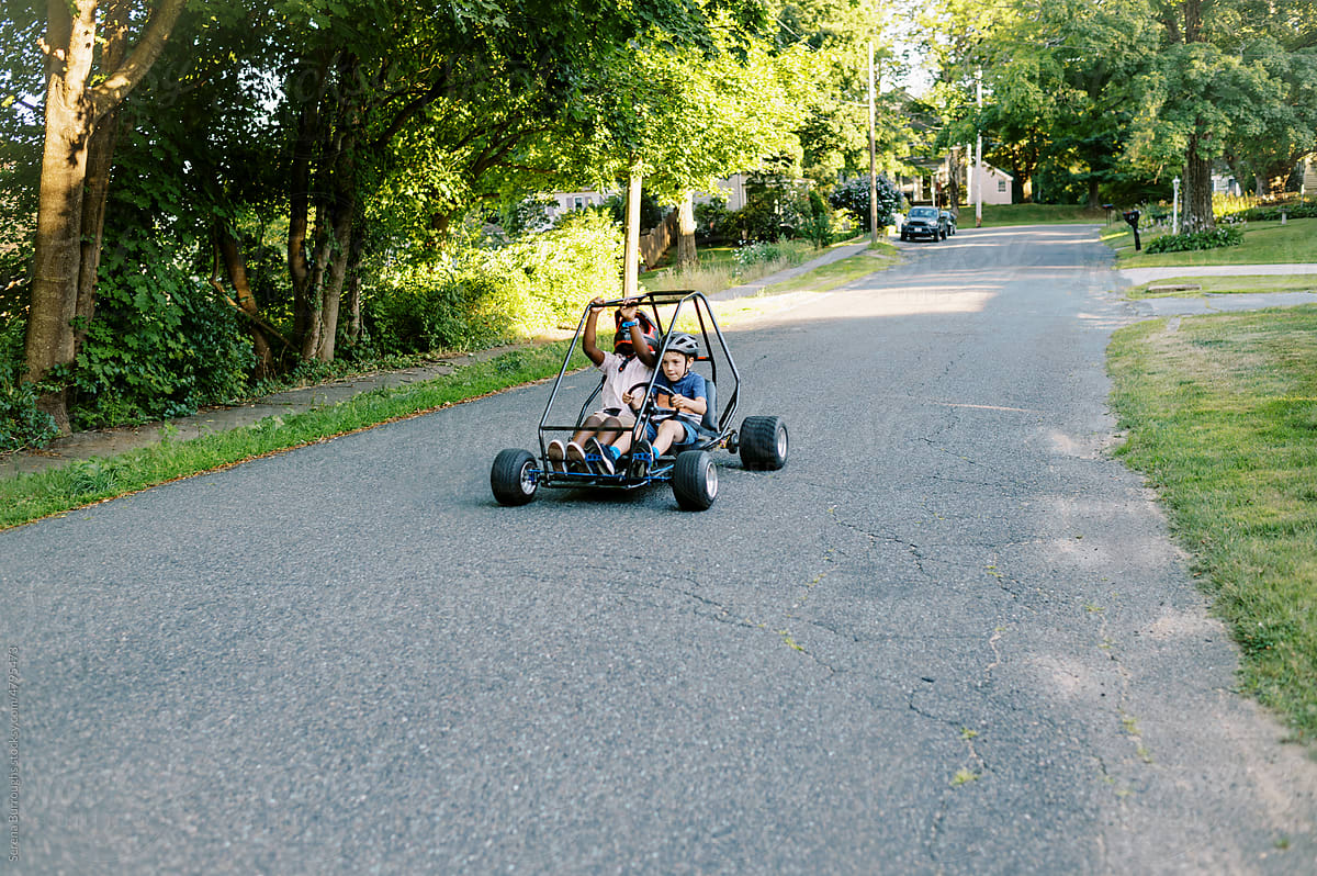 Two boys riding a go kart in their neighborhood street together