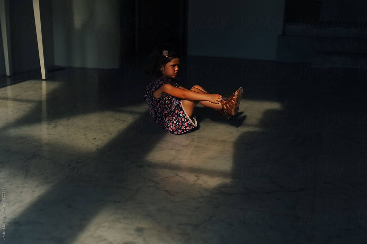 Child putting on her shoes while sitting on the floor.