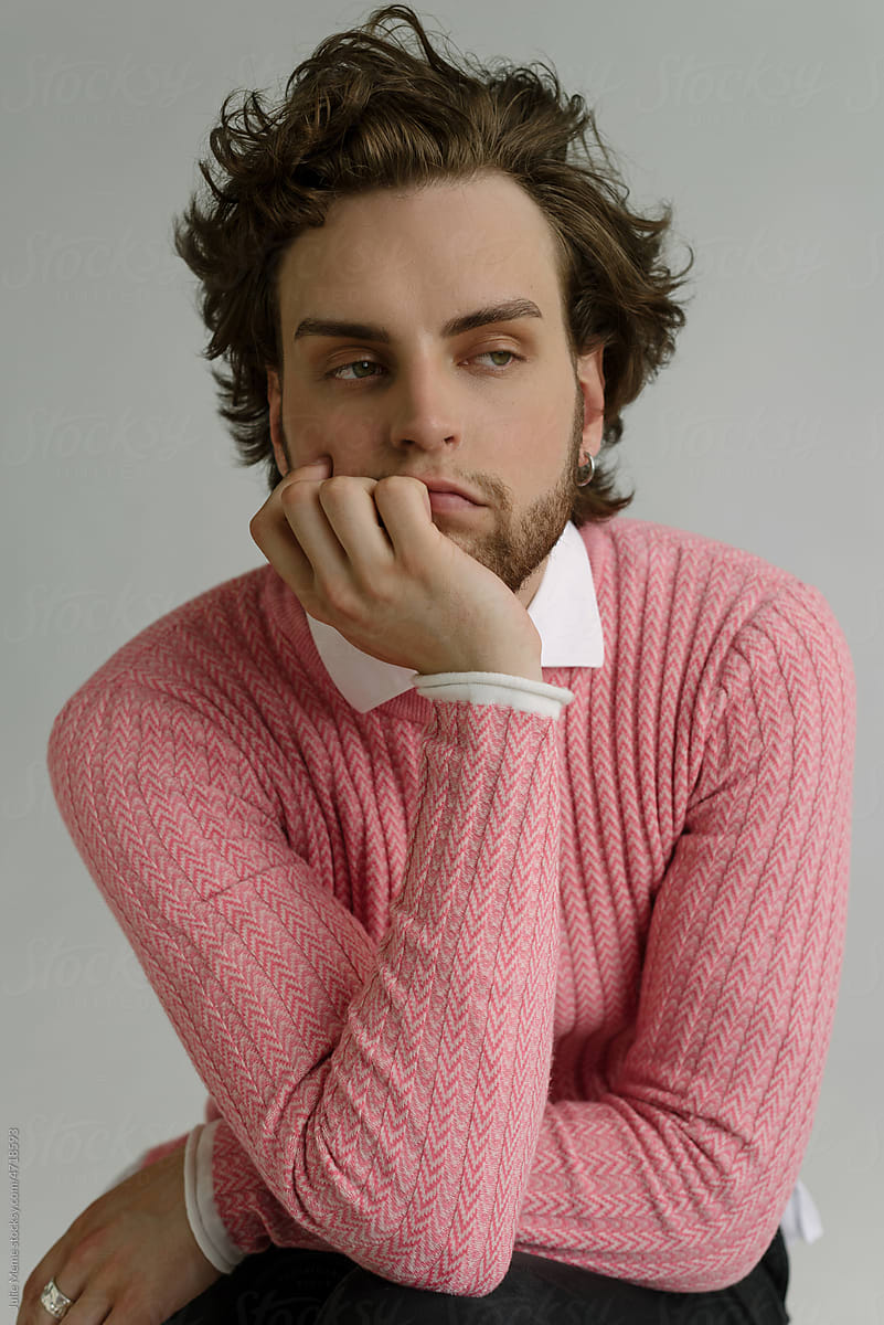 A thoughtful handsome guy with curly hair wearing a pink pullover