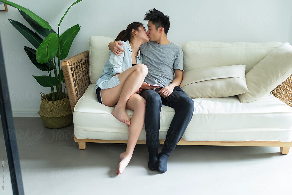 Young asian couple sitting in sofa and kiss at home by Bo Bo for Stocksy Un...